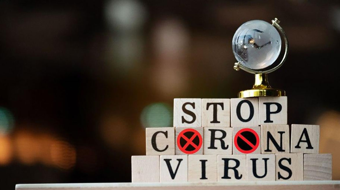 Ein kleiner Dekorationsglobus steht auf Bauklötzen. Die Bauklötze sind mit Buchstaben beschriftet. Sie ergeben den Satz "Stop Coronavirus".